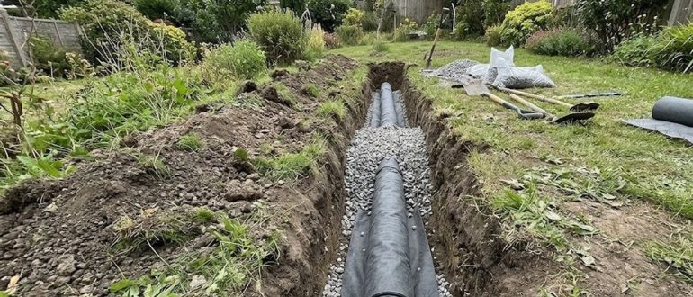 Траншея с дренажной трубой в геотекстиле на склоне участка